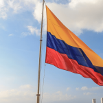 bandera de colombia izada con el cielo azul de fondo. Elecciones beneficios y obligaciones laborales